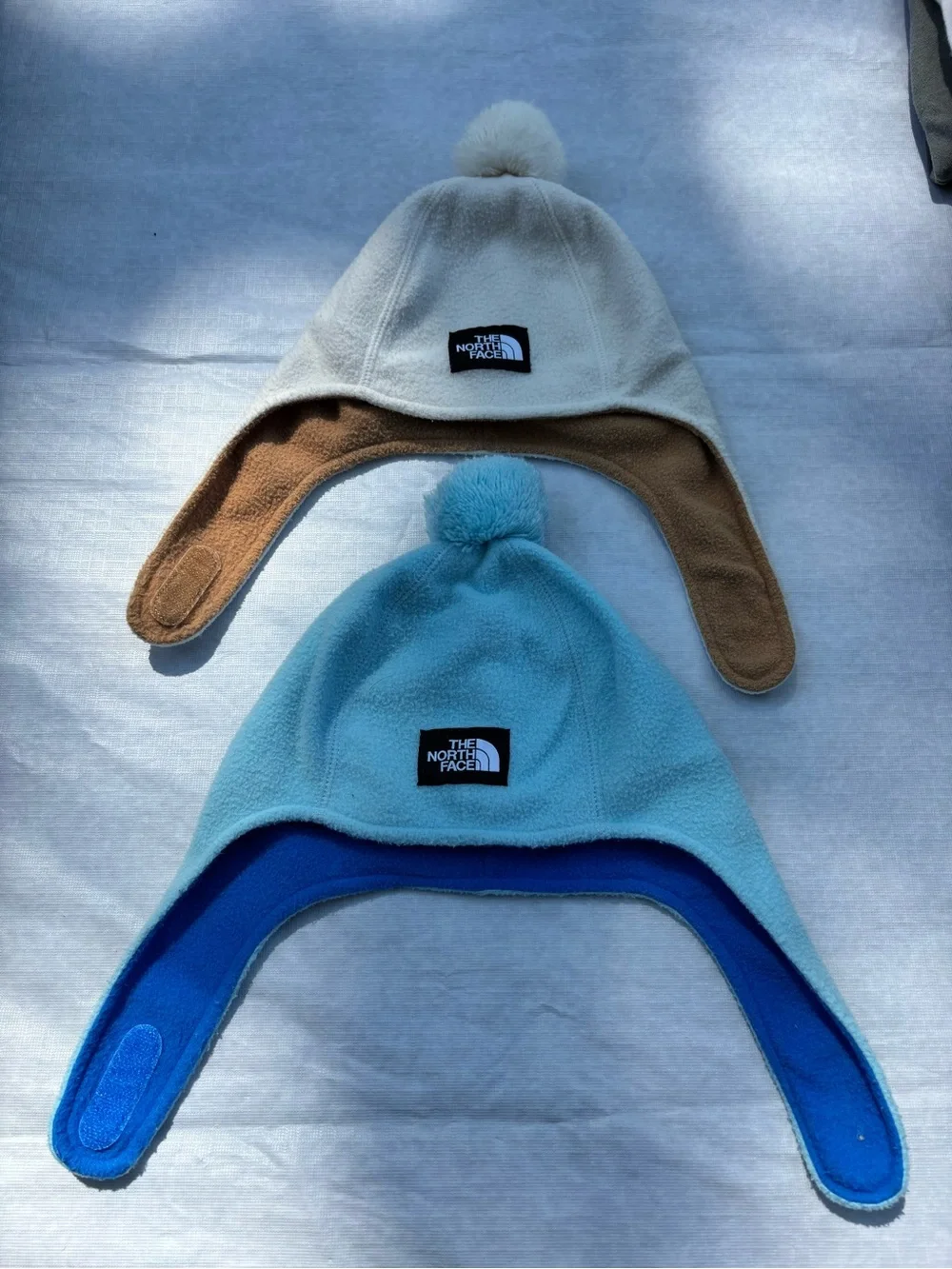 The North Face Fleece Earflap Pom-Pom Hats in Cream & Light Blue